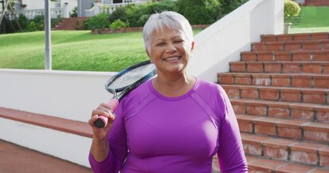 Senior woman joyfully holding tennis racket outdoors