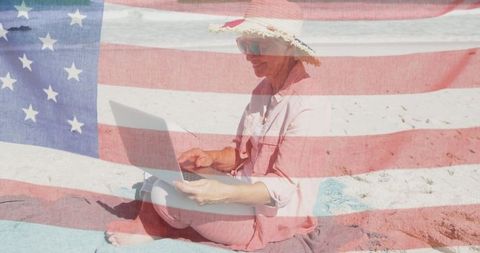 Patriotic Senior Woman Using Laptop on Beach Behind American Flag