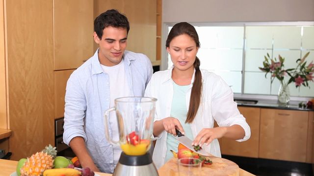 Couple engaged in preparing a healthy fruit smoothie in bright modern kitchen aesthetic. Freed-advertisement lifestyle series suitable for food blog posts, cooking websites, recipe cards, healthy living promotions, or home decor inspiration blogs, showcasing domestic leisure and bonding over meal prep.