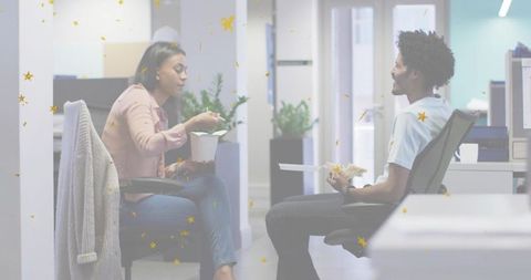 Coworkers eating lunch and chatting in modern open-plan office during casual midday break