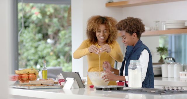 Mother and son enjoying quality time baking together in a bright modern kitchen. Around them, various baking ingredients are spread on the countertop, showcasing a delightful family activity. This visual is ideal for promoting family activities, cooking classes, parenting articles, and advertisements centered around home and lifestyle.