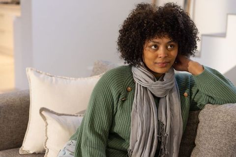 African american woman relaxing on sofa wearing green knit sweater and gray scarf