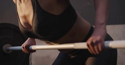 Woman lifting barbell closeup showing core strength, muscle tone and weight training