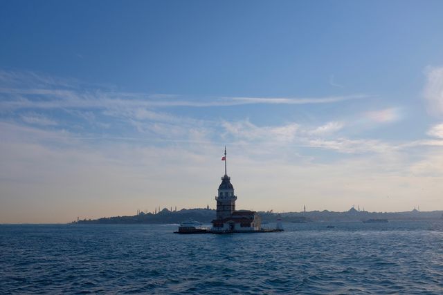 Maiden's Tower is seen in the calm sea water with a bright sunset sky. This stock photo is suitable for travel blogs, historical event promotions, holiday postcards, website design backgrounds, or educational materials highlighting historical landmarks in Turkey.