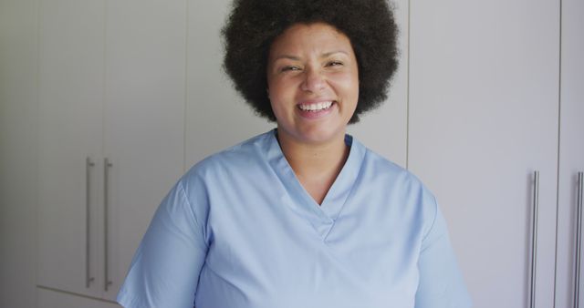 African American nurse wearing blue scrubs smiling warmly. Useful for representing healthcare professionals, hospital staff, and medical environments. Fits well in contexts related to medical care, nursing, patient support, and healthcare services marketing.