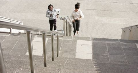 Pair jogging up urban concrete stairs with stainless steel railings in bright daylight