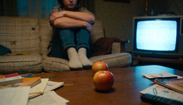 Teenage solitude on retro couch with glowing crt tv and apples on cluttered coffee table
