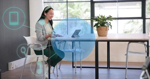 Working woman using tablet at modern coworking desk with wireless earphones and planter