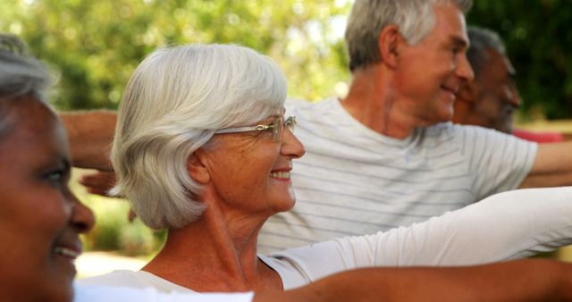 Seniors participating in outdoor arm exercises in a park. They seem happy and engaged, promoting a sense of community, fitness, and wellness among older adults. Great for use in advertisements promoting senior health, wellness programs, fitness routines for elderly, or active retirement lifestyles.