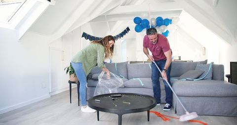 Couple Joyfully Cleaning Living Room After Birthday Celebration
