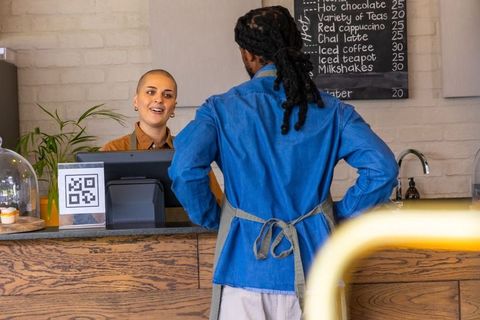 Smiling barista serving customer at cozy cafe counter with pos terminal and pastry dome