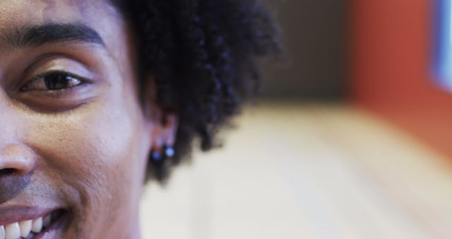 Close-up image captures a partial face of a young man with curly hair smiling brightly. Focuses on his eye and part of his smile. Suitable for concepts of confidence, happiness, and youthfulness.