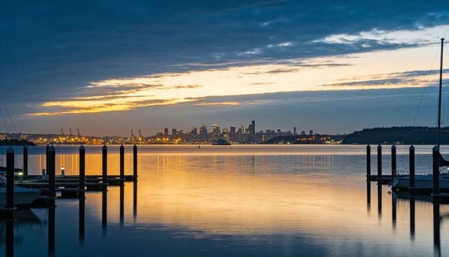 Reflecting harbor at dusk with illuminated city skyline, wooden piers and sailboats
