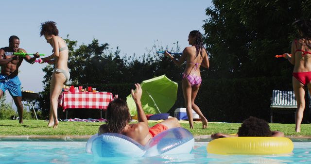 Biracial woman having fun playing with water guns in swimming pool. hanging out and relaxing outdoors in summer.