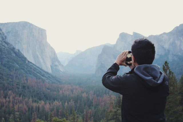 Image shows a man capturing the natural beauty of Yosemite National Park's mountains and forest. Ideal for travel blogs, nature photography showcases, outdoor adventure promotions, and travel agency ads.