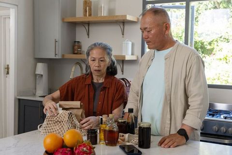 Senior asian couple unpacking groceries at marble kitchen island, preparing pantry jars