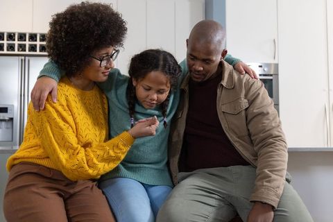 Parents comforting daughter examining small toy on kitchen countertop cozy family moment