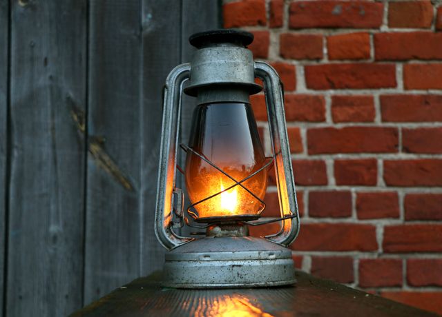 This nostalgic kerosene lantern emits a warm glow, emphasizing its vintage charm against a rustic brick wall. Ideal for use in articles or posts related to retro decor, outdoor lighting, antique collections, or creating cozy ambiance. Suitable for advertising home decor, historical reenactment props, or rustic-style product designs.