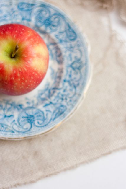 Red apple on a decorative blue patterned plate, perfect for illustrating fresh food, healthy eating, vintage kitchenware, or artistic table settings. Suitable for websites, blog posts, recipe books, or magazine articles about nutrition and lifestyle.