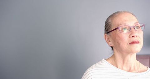 Senior woman in contemplation, gazing at gray wall