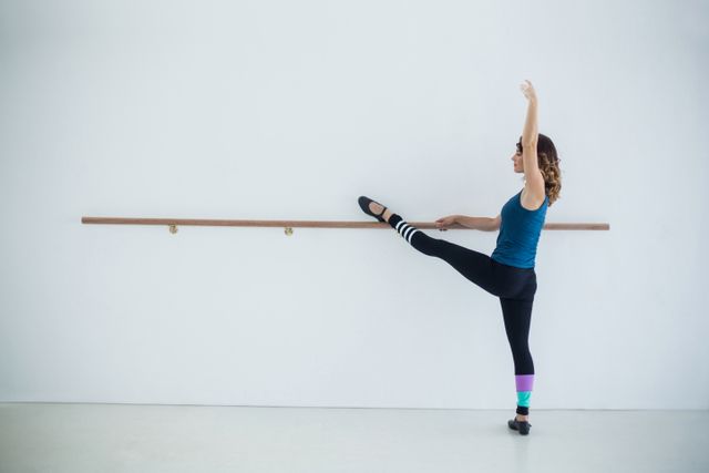 Ballet dancer stretching at barre in dance studio, demonstrating flexibility and grace. Ideal for use in articles or advertisements related to dance, fitness, training, and wellness. Perfect for illustrating concepts of discipline, practice, and physical fitness.