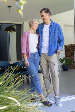 Couple standing close together on patio threshold smiling and embracing in sunlit modern home