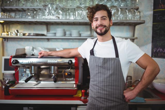 Portrait of smiling waiter standing with hand on hip at counter in cafÃ©