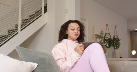 Relaxed woman on couch using tablet with stylus in cozy modern living room interior