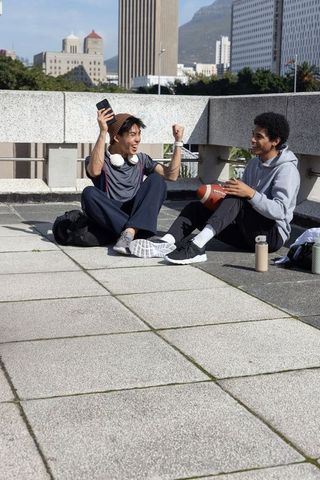 Urban friends celebrating victory on rooftop with smartphone and football