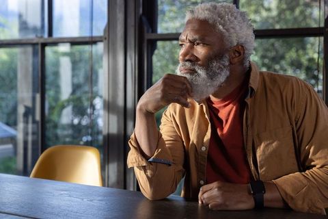 Contemplative senior african american man sitting at table near window with smartwatch