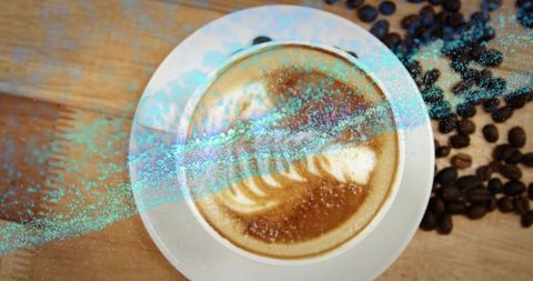 Top-down latte art in white cup on rustic wooden table with scattered coffee beans