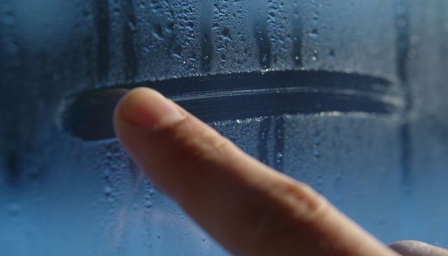 Fingertip wiping condensation on glass leaving clear horizontal line with cool blue droplets