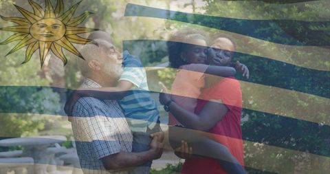 Multi-generational family hugging in park with faded uruguayan sun flag overlay