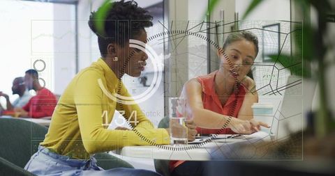Women collaborating over laptop and documents with digital hud in modern coworking lounge