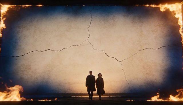 Walking couple approaching camera backlit by cracked wall framed by flames