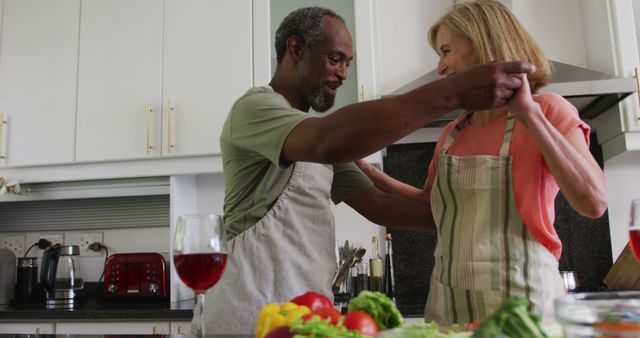 Diverse senior couple wearing aprons dancing while preparing food in kitchen - Download Free Stock Photos Pikwizard.com