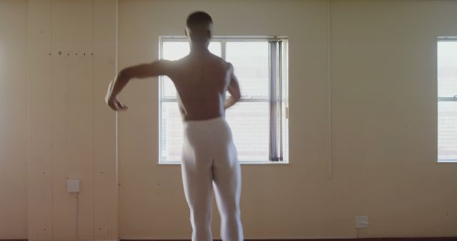 Male ballet dancer practicing graceful movements in bright, sunlit studio setting. Ideal for use in projects related to performing arts, ballet training, professional dance, dance routines, and physical fitness.