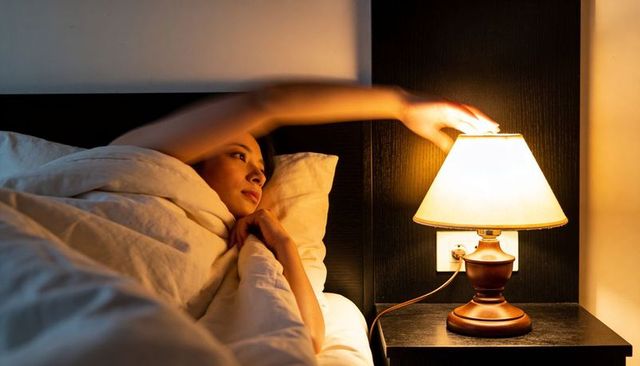 Woman reaching to turn off bedside lamp in cozy minimalist bedroom nighttime warm glow