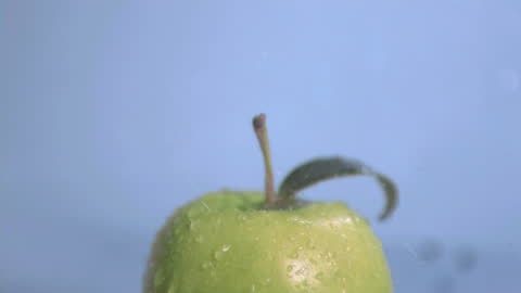 Green Apple Covered in Rain Droplets Against Blue