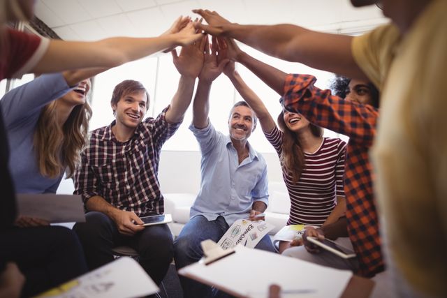 Group of cheerful business people giving high five while sitting in a creative office. Ideal for illustrating teamwork, collaboration, and positive office culture. Suitable for use in business presentations, team-building materials, and motivational content.