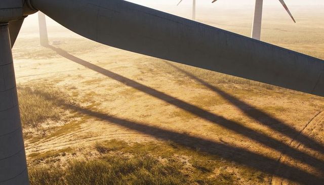 Wind turbine blade casting long shadows over dry prairie at sunrise renewable energy