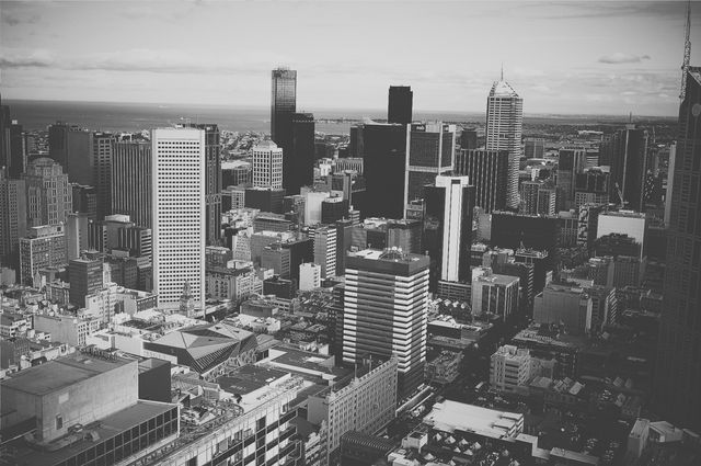This black and white photo shows an aerial view of a bustling urban city with tall skyscrapers and various buildings. It is great for presentations on urban development, city planning, architecture, and real estate promotions. This photo communicates the concept of a modern, busy metropolitan area and can be used in articles or adverts emphasizing city life and development.