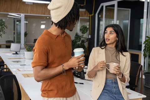 Casual coworkers sharing coffee while discussing business data in open office