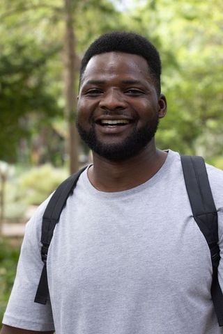 Confident african american student smiling on campus wearing backpack light gray t-shirt
