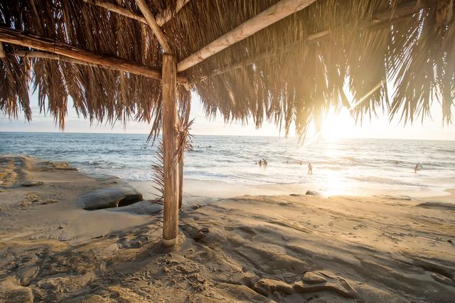 Capturing a breathtaking sunset view through a rustic tiki hut on a serene tropical beach. Perfect for travel brochures, vacation advertisements, or blog posts about relaxation, tropical destinations, and coastal getaways.