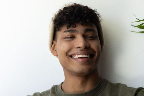 Young african american man smiling in knit beanie, warm candid headshot with minimal greenery