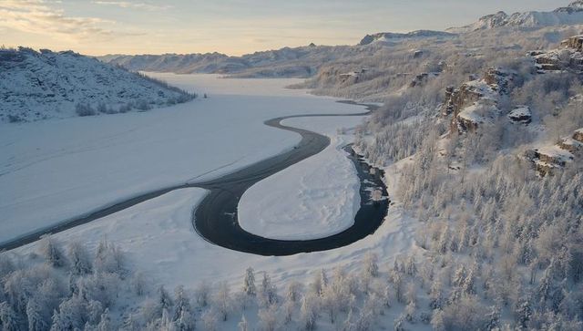 Aerial view of meandering open channel winding through snow-covered boreal river valley