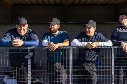 Coaches leaning on dugout rail reacting to play and sharing laughter