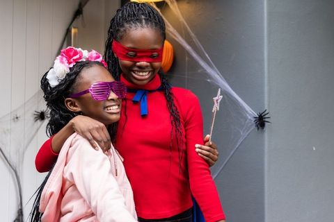 Joyful african american sisters wearing halloween costumes on cobwebbed porch, autumn fun