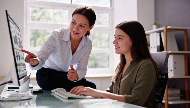 Senior woman mentoring colleague while analyzing business charts on desktop in office